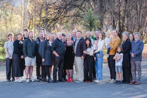 Large extended family group posing together outdoors in autumn setting with trees in background.