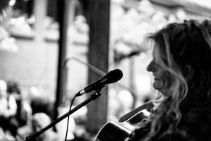 A musician performs on stage with a microphone and guitar in black and white.