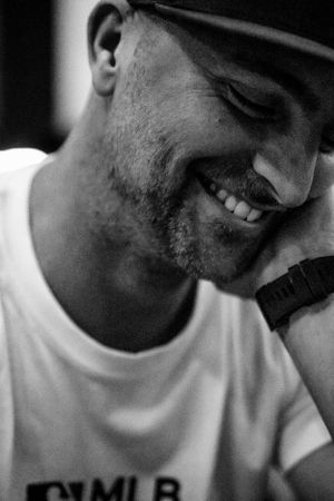 A close-up black and white portrait shows a smiling person wearing a cap.