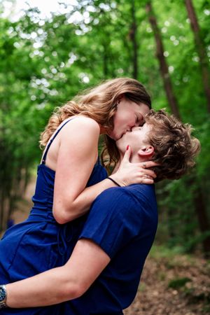 A romantic embrace between two people in blue clothing against a green forest backdrop.