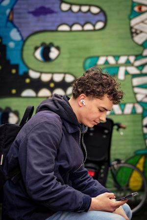 Person in navy sweatshirt looking at phone against colorful graffiti wall.