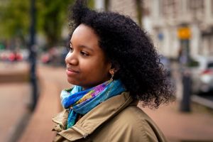 Woman with natural curly hair and turquoise scarf walking outdoors.