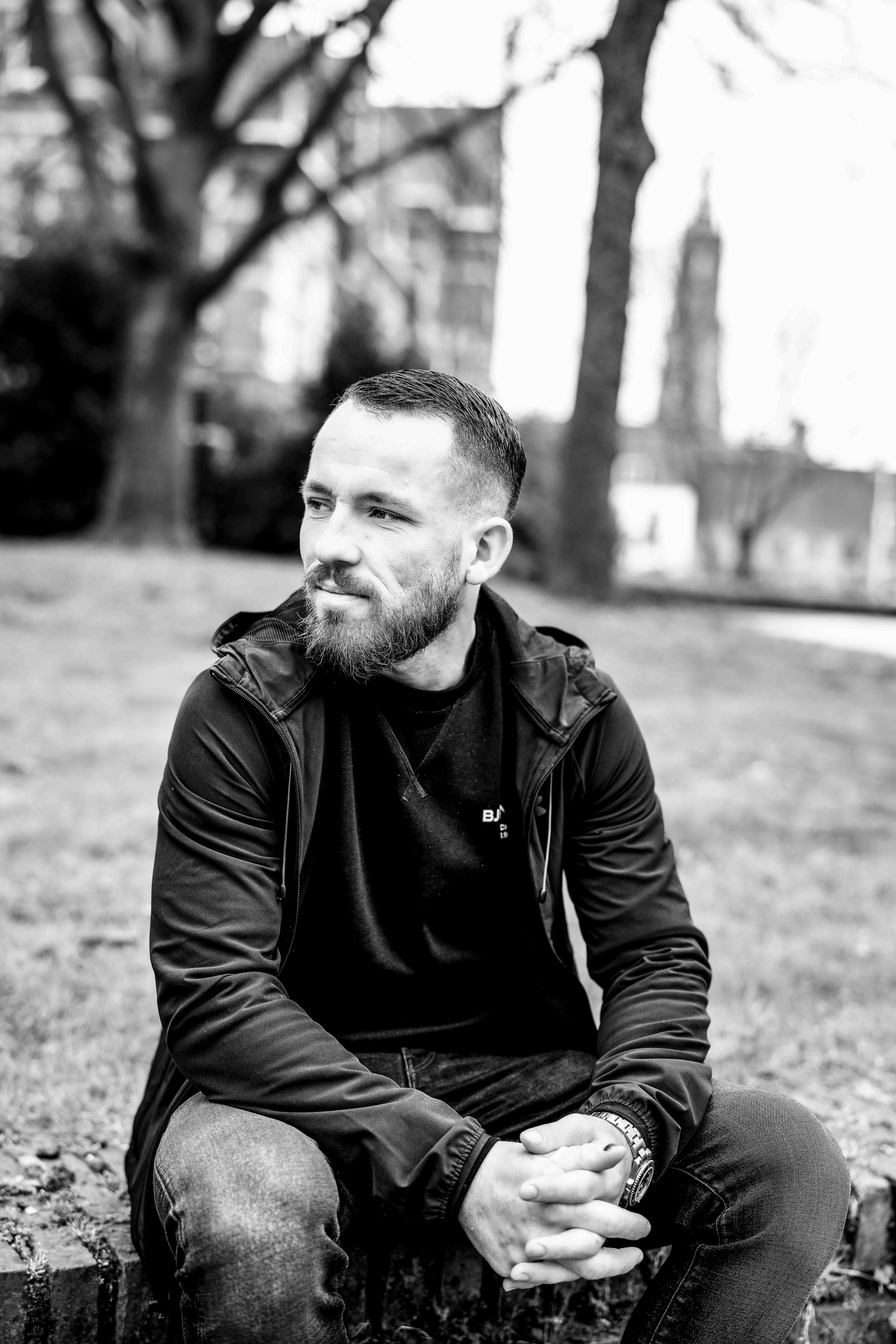 Person in black jacket sitting outdoors looking contemplative.