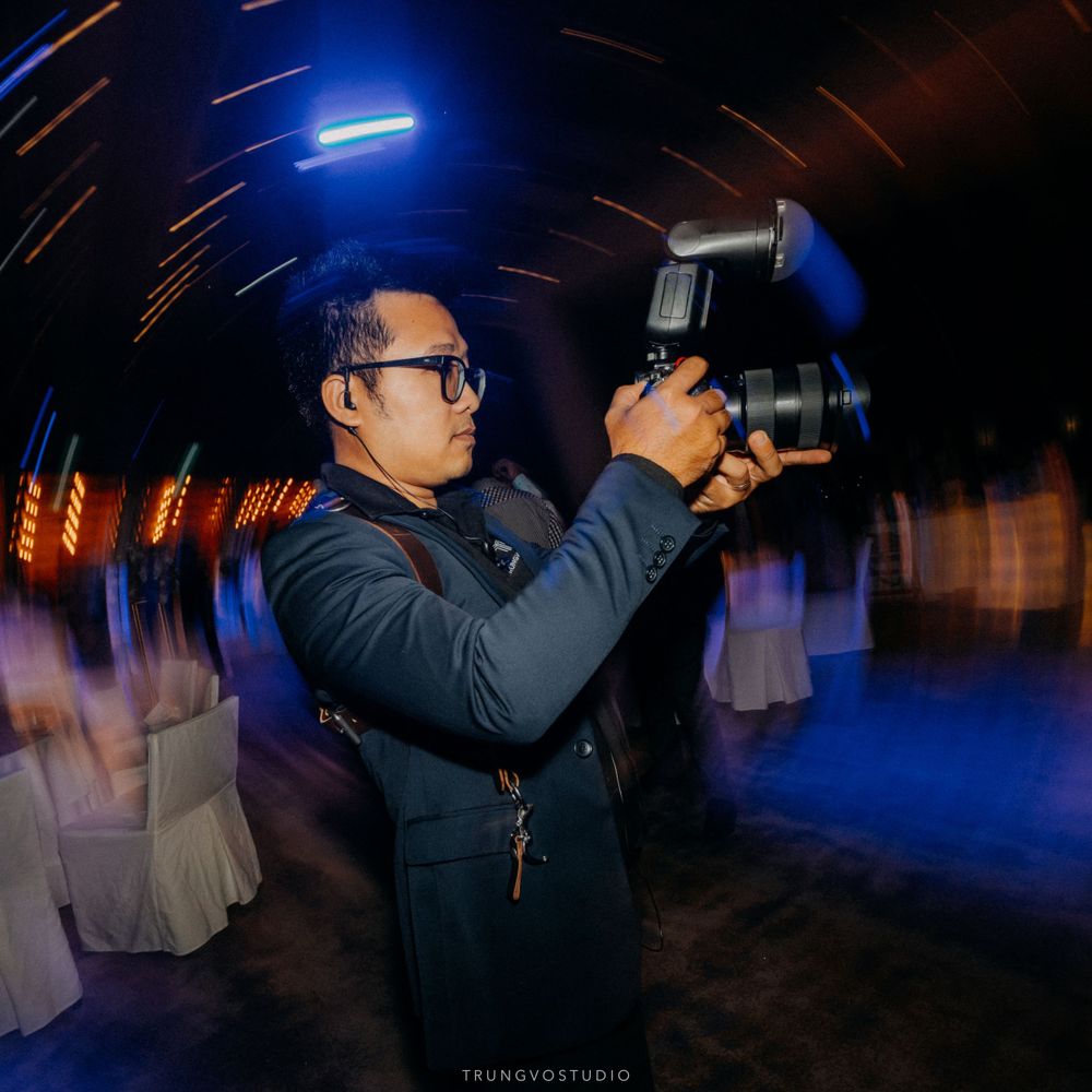 Photographer capturing moments at a wedding with a camera flash in a dark blue-lit venue.