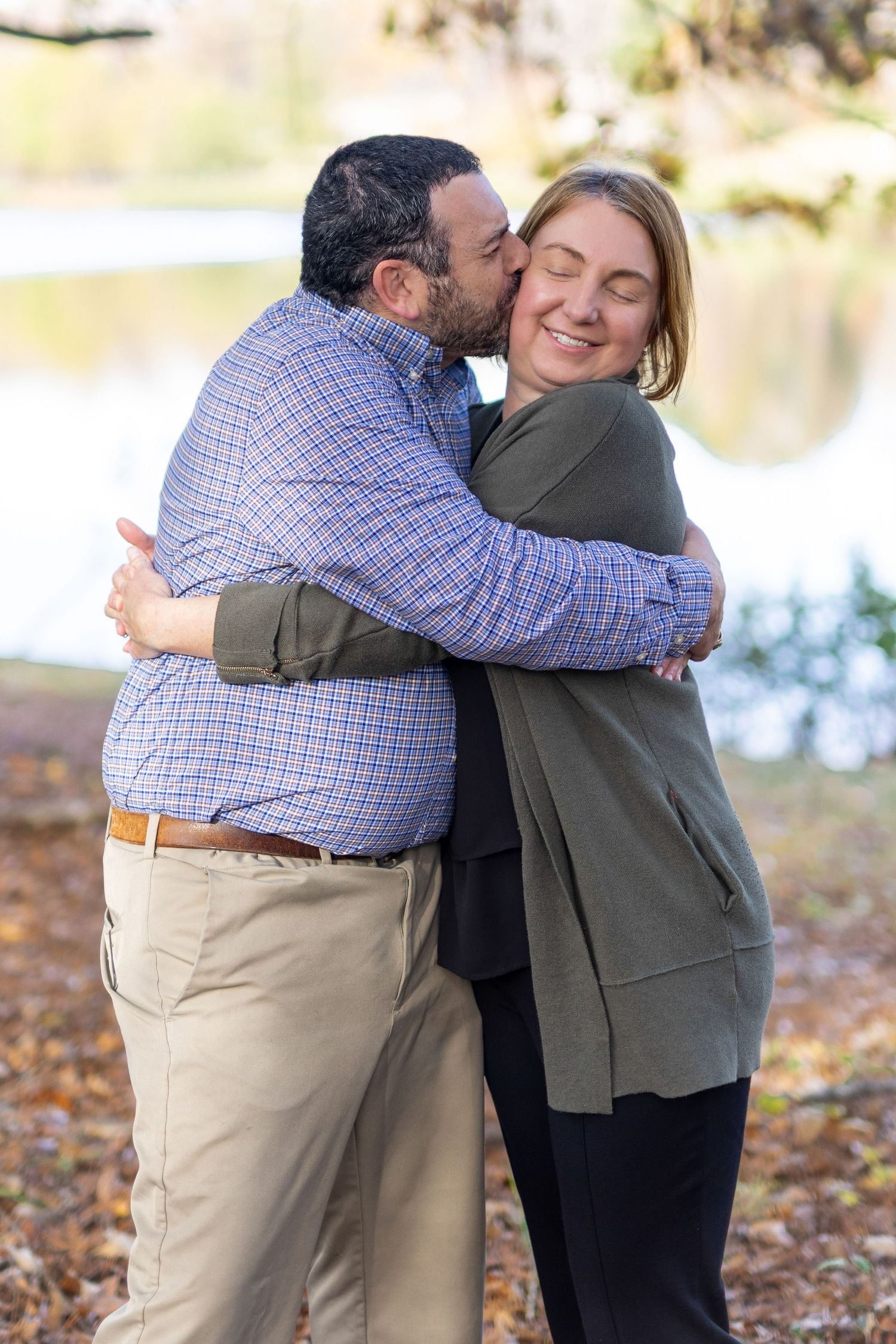 Playful hug and kiss during romantic couples shoot in Essex County park.