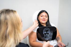 Esthetician analyzing client skin with facial scanning device during beauty consultation in modern salon.