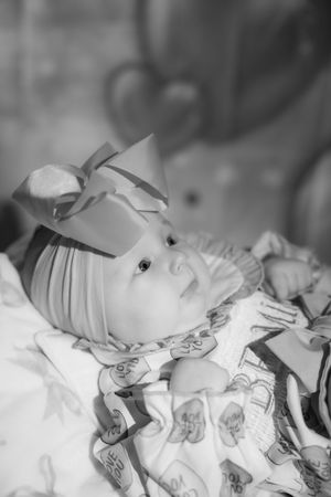 Black and white photo of a newborn baby girl wearing a bow headband, wrapped in a patterned blanket.