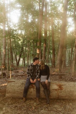 Three people sit together on a fallen log in a sunlit forest with warm autumn tones and dappled lighting.