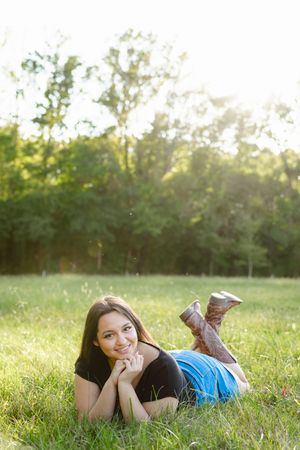 Person lying in green grass field during golden hour sunset with natural bokeh background.