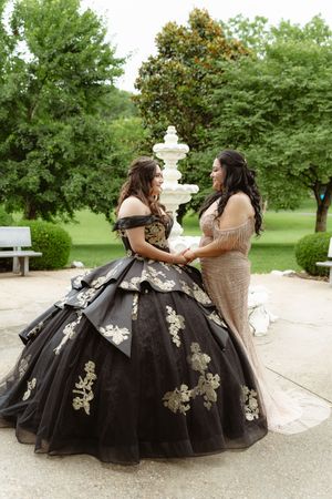 Two people in elegant black and white ballgowns sit together in a garden setting sharing a tender moment.