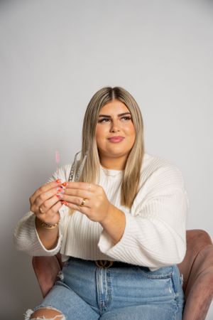 Person in white sweater holding pink skincare tools against gray background.