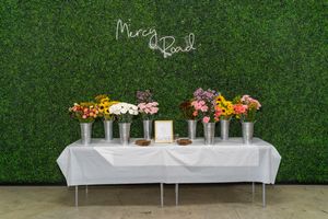 Elegant outdoor wedding ceremony setup with white chairs, floral arrangements, and a lush green hedge backdrop.