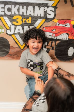 Excited boy at Beckham's 3rd birthday party with monster truck theme banner, laughing joyfully.