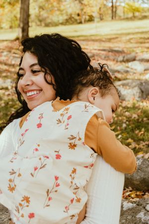 A joyful autumn family photoshoot shows a mother and baby sharing a tender moment among fallen leaves.