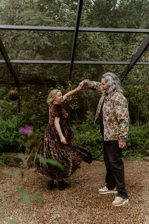 A couple dances playfully together in a forest setting surrounded by woodchips and greenery.