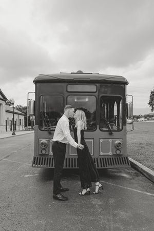 A romantic black and white photo of a couple sharing a tender moment in front of a vintage trolley bus.
