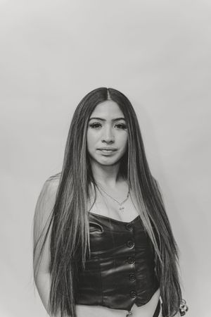 Black and white portrait of a young woman with long straight hair wearing a leather top and delicate necklace.