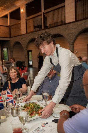 A waiter serves a colorful salad to guests at a formal dining event decorated with British flags.