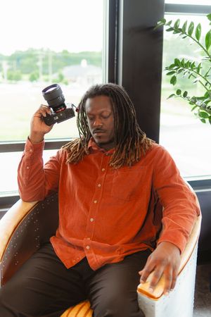 Person in orange button-down shirt sitting in chair by window with dreadlocks shown in multiple poses.