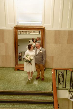 A couple shares a tender moment in front of a large mirror in a room with green carpet.