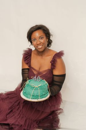 Woman in burgundy tulle dress holding a teal 40th birthday cake, smiling against a white background.