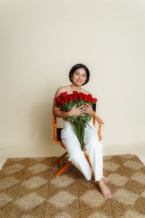 Four sequential photos show someone in white sitting on a wooden chair holding a bouquet of red roses against a beige wall.