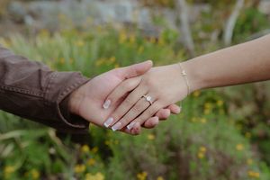 Two hands reaching out to hold each other against a blurred green natural background.