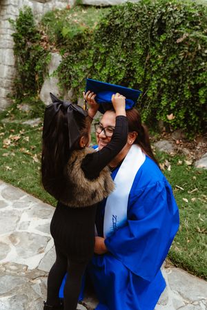 Three people embrace in a garden setting with one wearing a bright blue graduation gown.