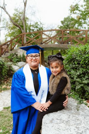 A graduation celebration photoshoot in a garden setting with blue academic regalia against a stone wall background.