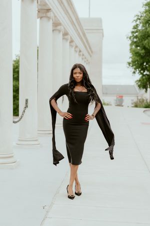 A fashion photoshoot in a white columned corridor features a model in a black dress and leather jacket striking dynamic poses.