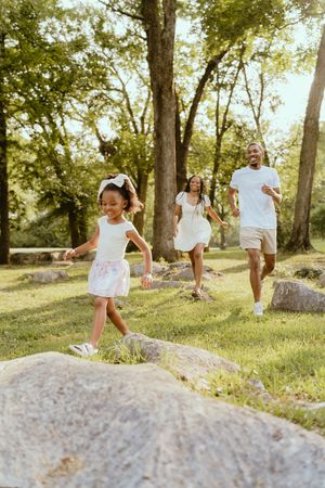 A sequence of images showing someone in white clothing leaping gracefully across rocks in a sunlit wooded area.