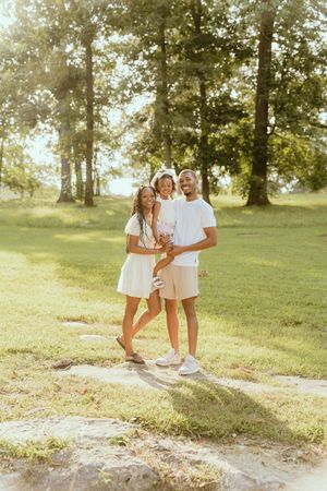 Three connected photos show a couple enjoying a sunny day on a grassy hill beneath tall trees in warm lighting.