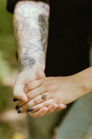A series of hands holding each other in sequence, showing tattoos, black nail polish, and a small ring.