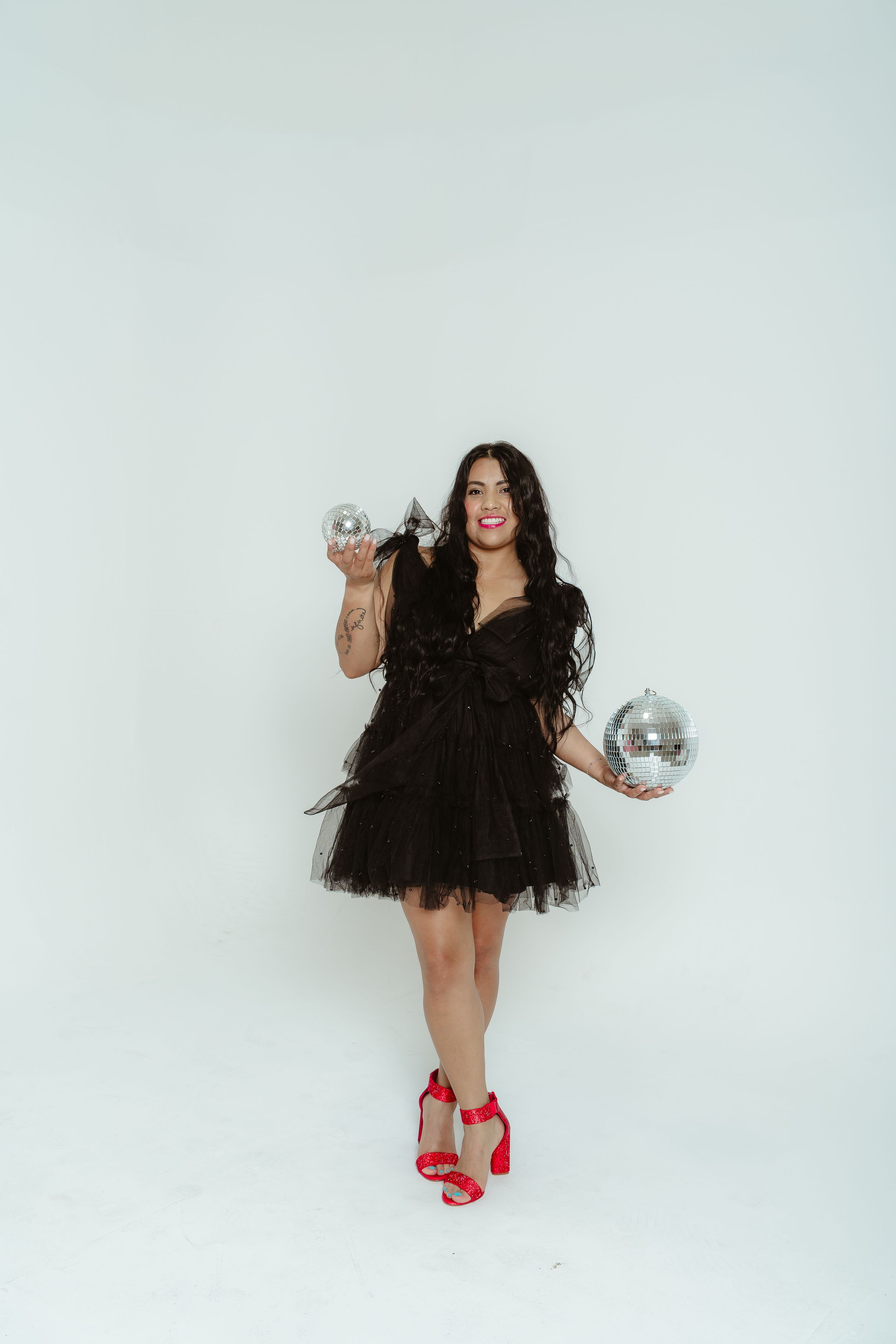 Festive party scene with silver disco balls and a black tulle dress against a white backdrop.