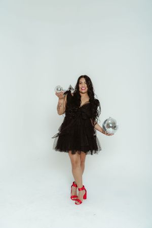 Festive party scene with silver disco balls and a black tulle dress against a white backdrop.