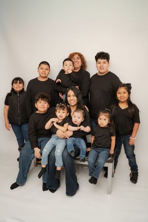 Large family portrait with adults and children wearing matching black shirts and jeans posed together in a studio.