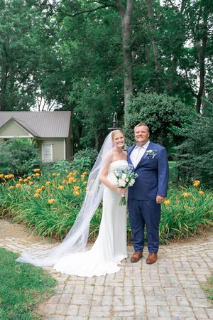 Bride and groom pose on brick path surrounded by orange day lilies and lush greenery at outdoor garden wedding.