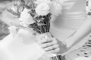 Black and white photo of a bride holding a white rose bouquet with a wedding ring visible on her finger.