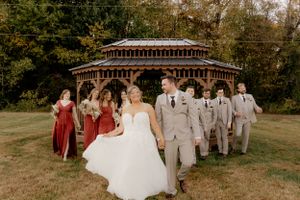 Wedding party poses in front of a wooden gazebo with bridesmaids in burgundy and groomsmen in gray suits.