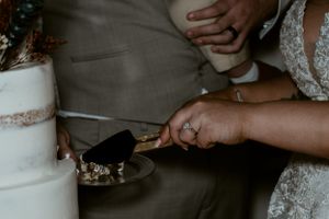 Close-up shot of hands cutting an elegant white wedding cake.
