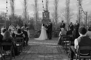 Black and white outdoor wedding ceremony on a brick patio with guests seated in chairs facing the couple at the altar.
