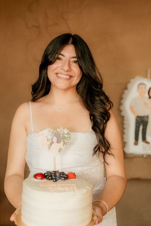 A white frosted cake decorated with fresh berries is held against a warm brown background.