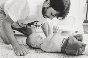 Black and white photo of a father lovingly leaning over his newborn baby lying on a blanket.