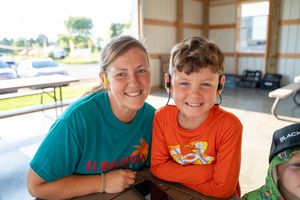 A smiling woman in a teal shirt and a boy in an orange shirt pose together at an outdoor event.