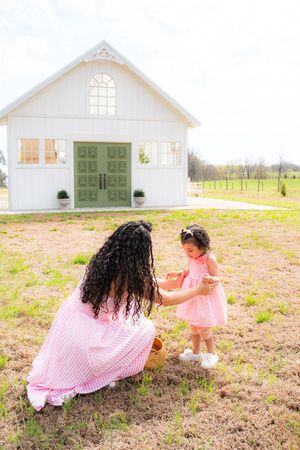 Mother and toddler daughter in matching pink dresses sharing a basket outdoors near a white barn.