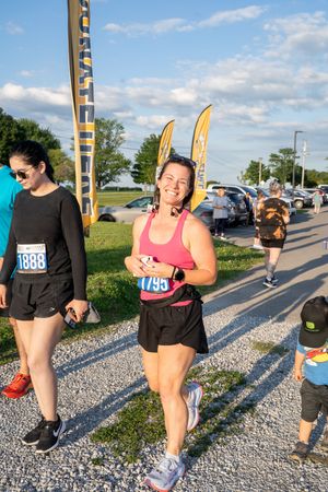 Smiling woman wearing bib number 1795 runs in an outdoor road race on a sunny day.