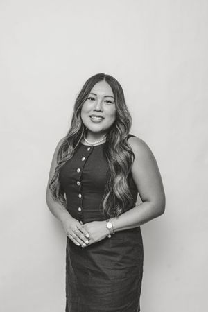 Black and white professional headshot of a smiling woman in a sleeveless dress with wavy hair.