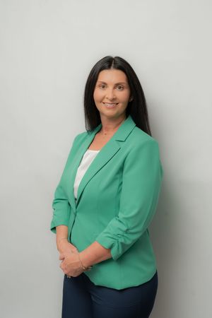 Professional woman in green blazer and white top smiling confidently against a light gray background.