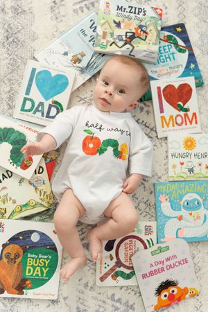 Baby lying surrounded by colorful children's board books wearing a half way one onesie milestone photo.