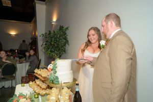 Wedding couple cutting cake at reception surrounded by dessert display.